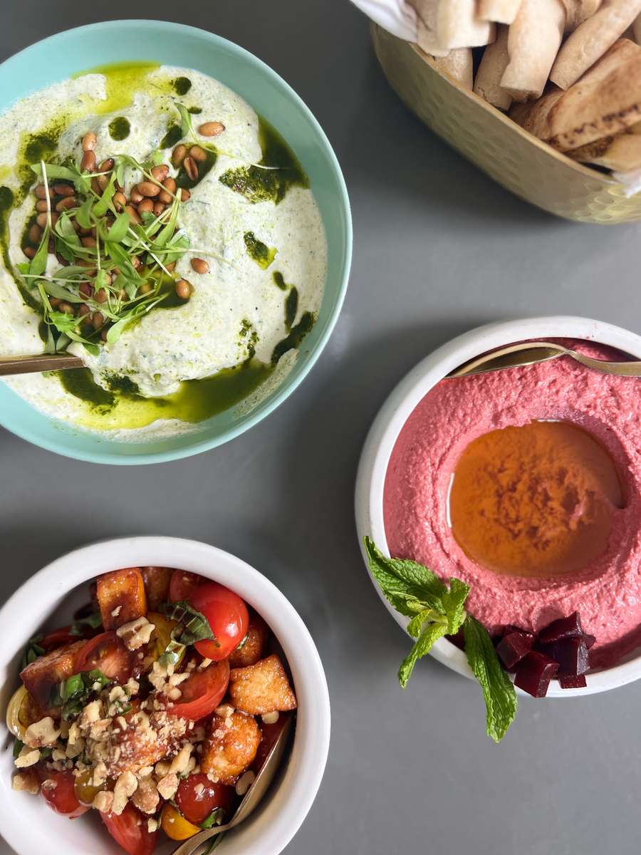 Trio of authentic Lebanese favorites featuring creamy hummus, vibrant beet hummus, and a fresh grain bowl with vegetables at Lira House in Wynwood, Miami.