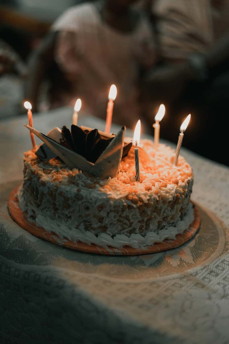 Birthday cake topped with chocolate decorations and lit candles, glowing warmly in a celebratory setting.
