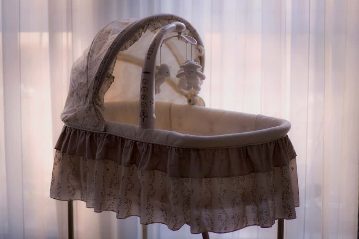 Softly lit baby bassinet with lace trim and a hanging mobile, set against sheer curtains for a serene nursery ambiance.