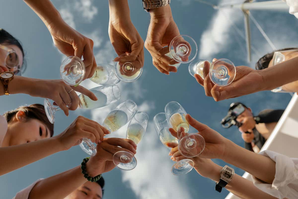 People raising champagne glasses in a celebratory toast under a clear blue sky, creating a festive and joyful atmosphere.