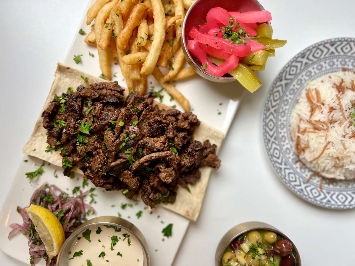 Charcoal-grilled Lebanese beef shawarma served over warm pita with crispy fries, house pickles, garlic sauce, and fresh herbs at Lira House in Wynwood, Miami.