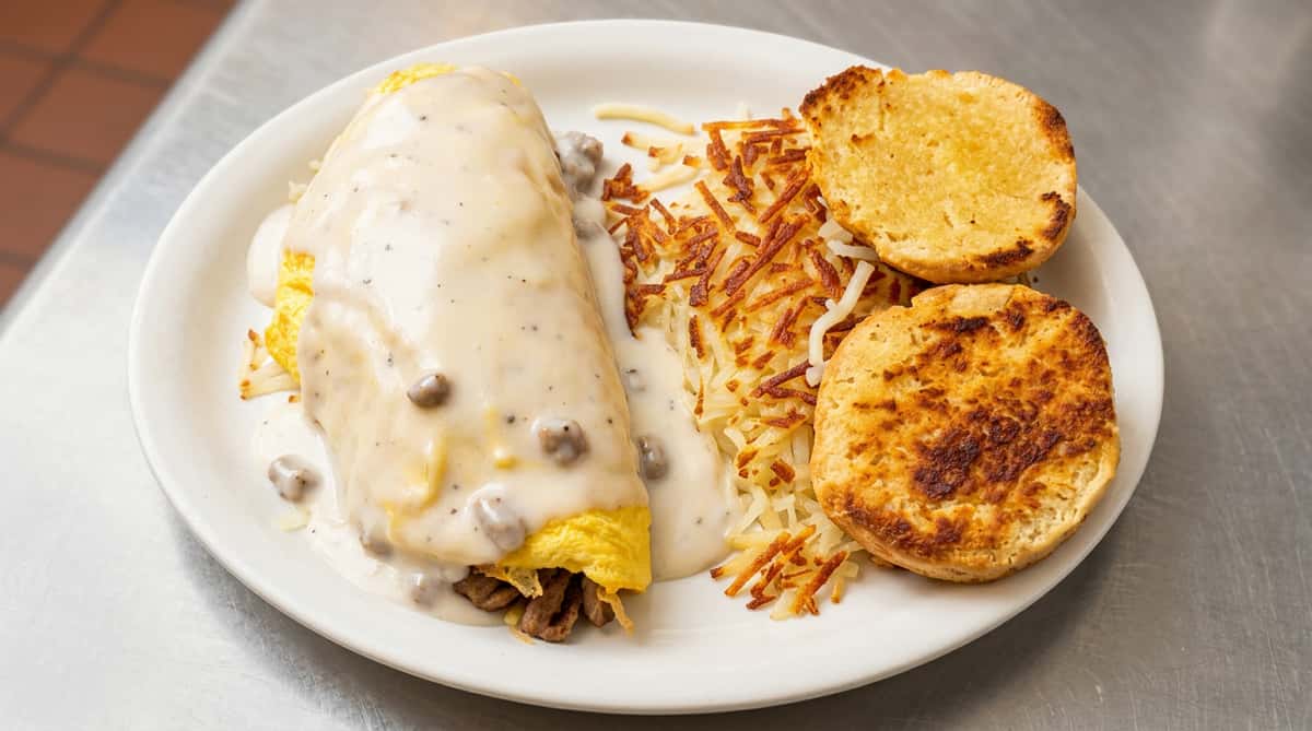 Breakfast platter with an omelette covered in sausage gravy, hash browns, and two round biscuits.