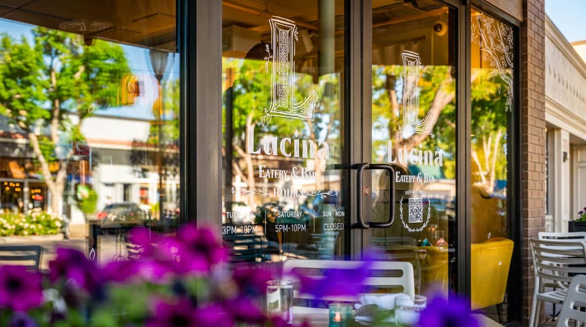 Glass entrance of Lucina Eatery & Bar with white lettering and business hours reflected in the glass.