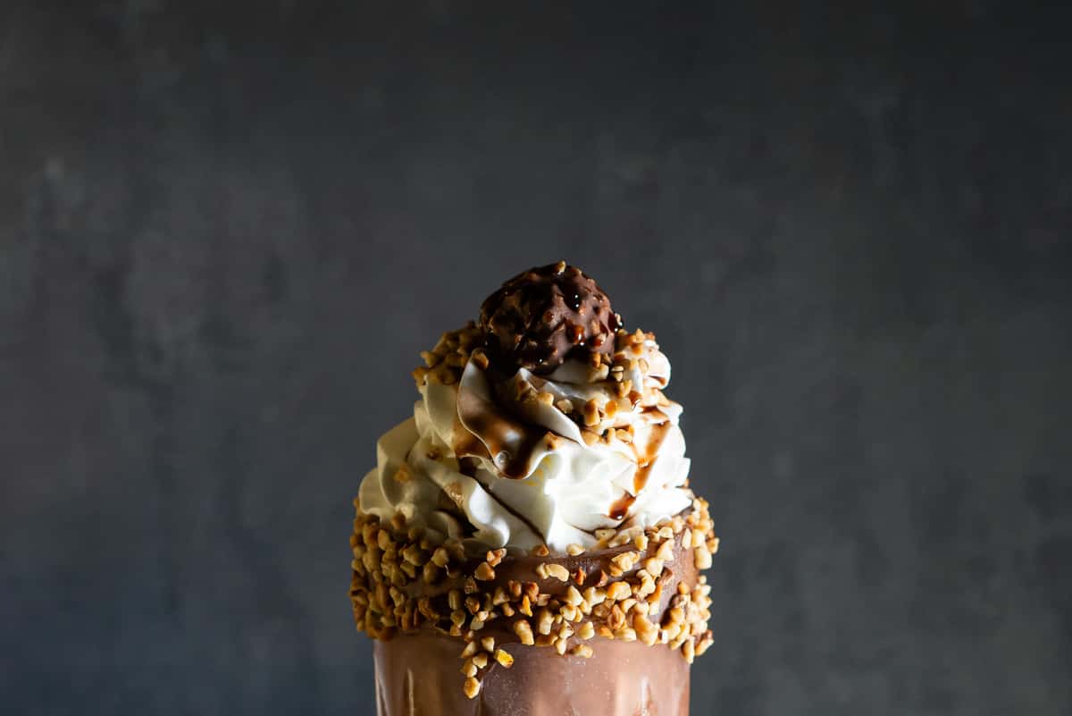 Indulge in a rich chocolate milkshake topped with whipped cream and nuts, perfect for dessert lovers.