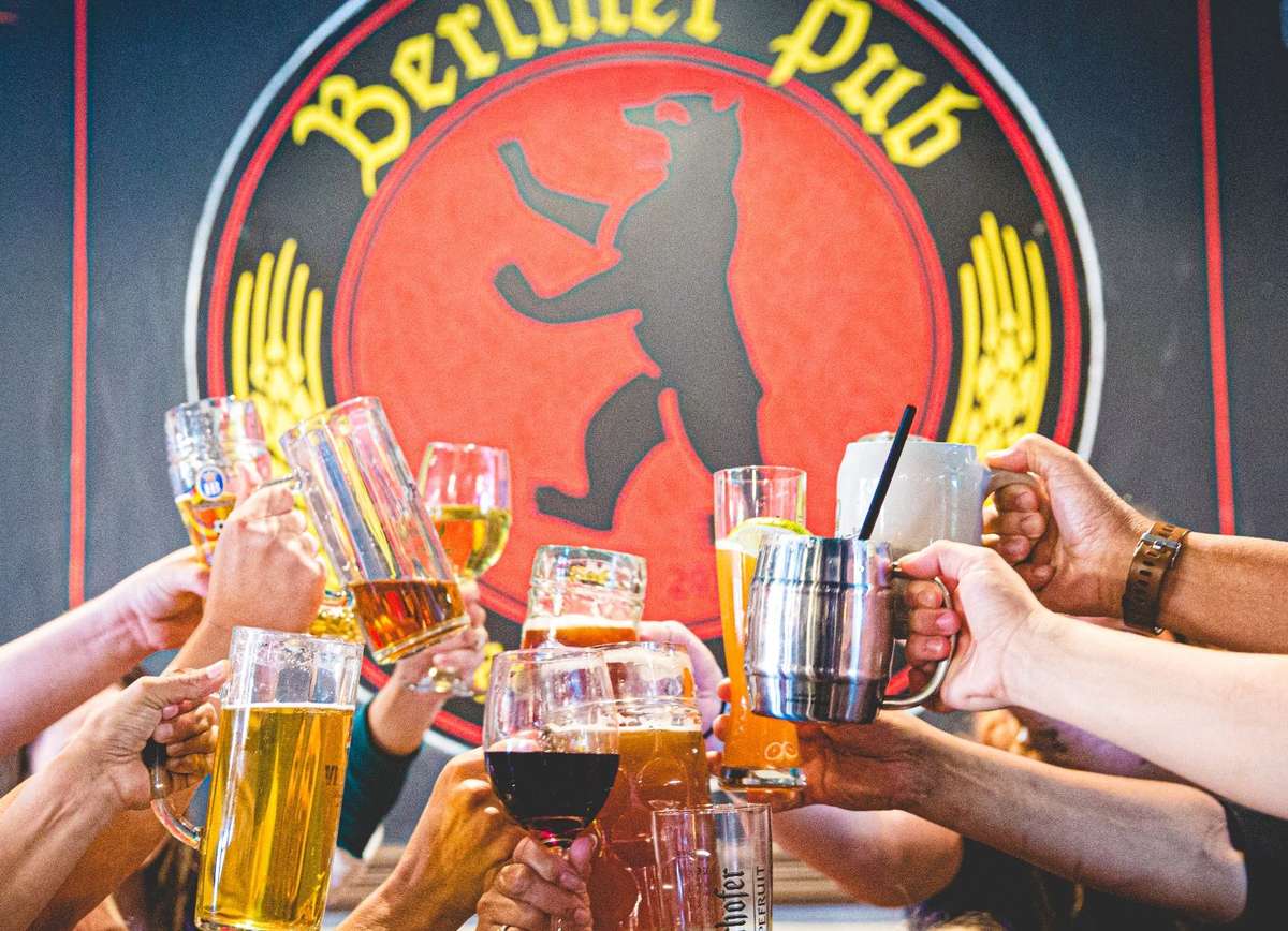 Friends raising beer steins, cocktails, and wine glasses in a celebratory toast at Berliner Pub, creating a lively atmosphere for drinks, dining, and social gatherings.