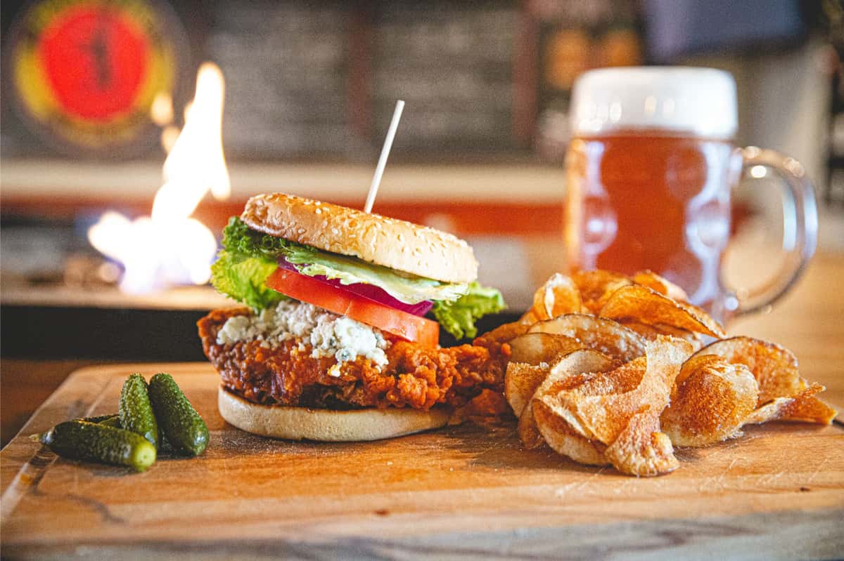Buffalo chicken sandwich topped with lettuce, tomato, and pickles on a toasted bun, served with crispy potato chips at Berliner Pub.