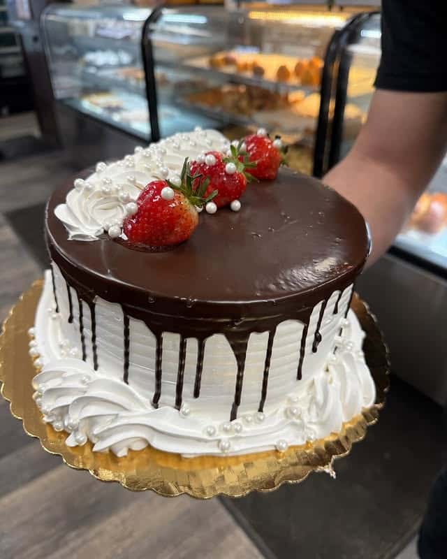 Elegant chocolate drip cake topped with fresh strawberries, whipped cream swirls, and decorative pearl accents at Brazilian Family Bakery.