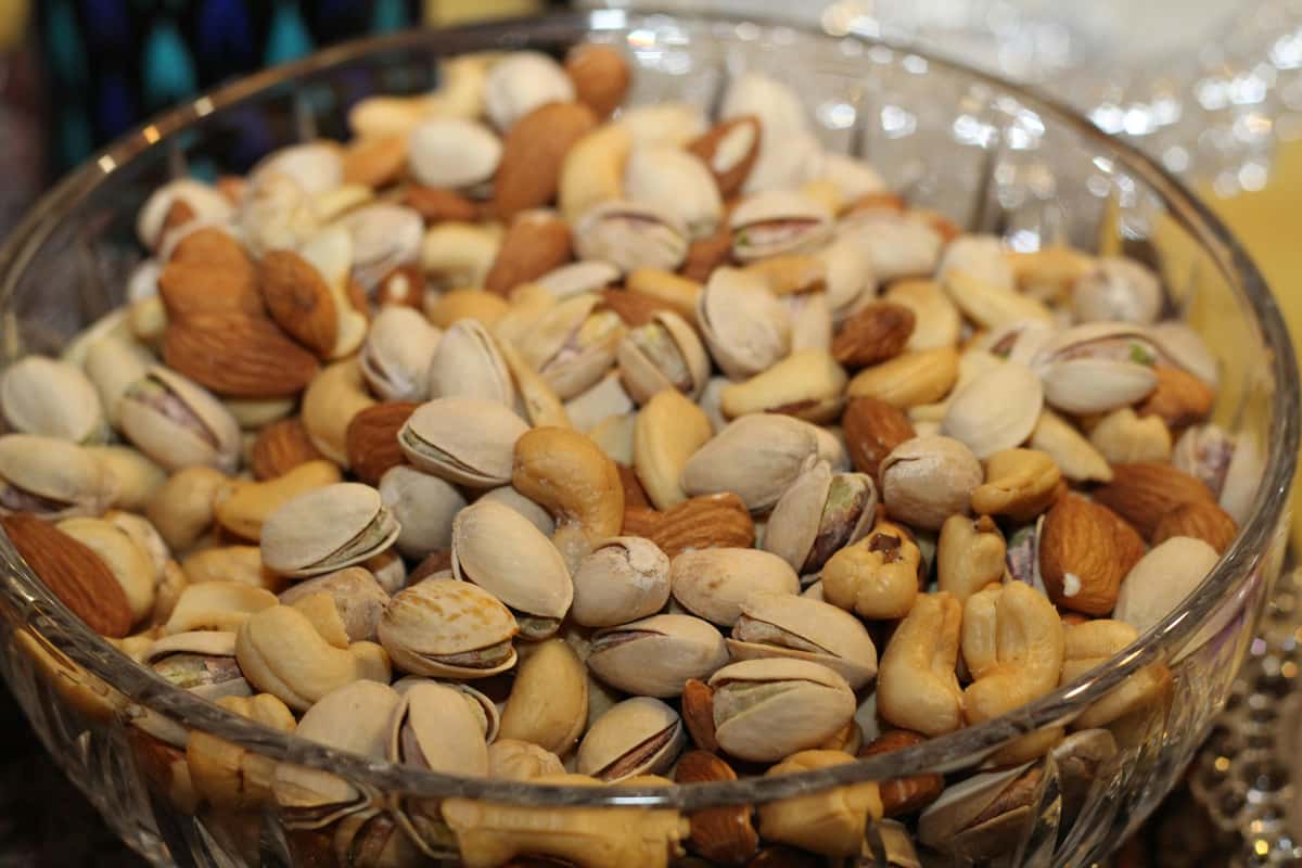 A glass bowl filled with a colorful assortment of mixed nuts, including pistachios, cashews, almonds, and hazelnuts.