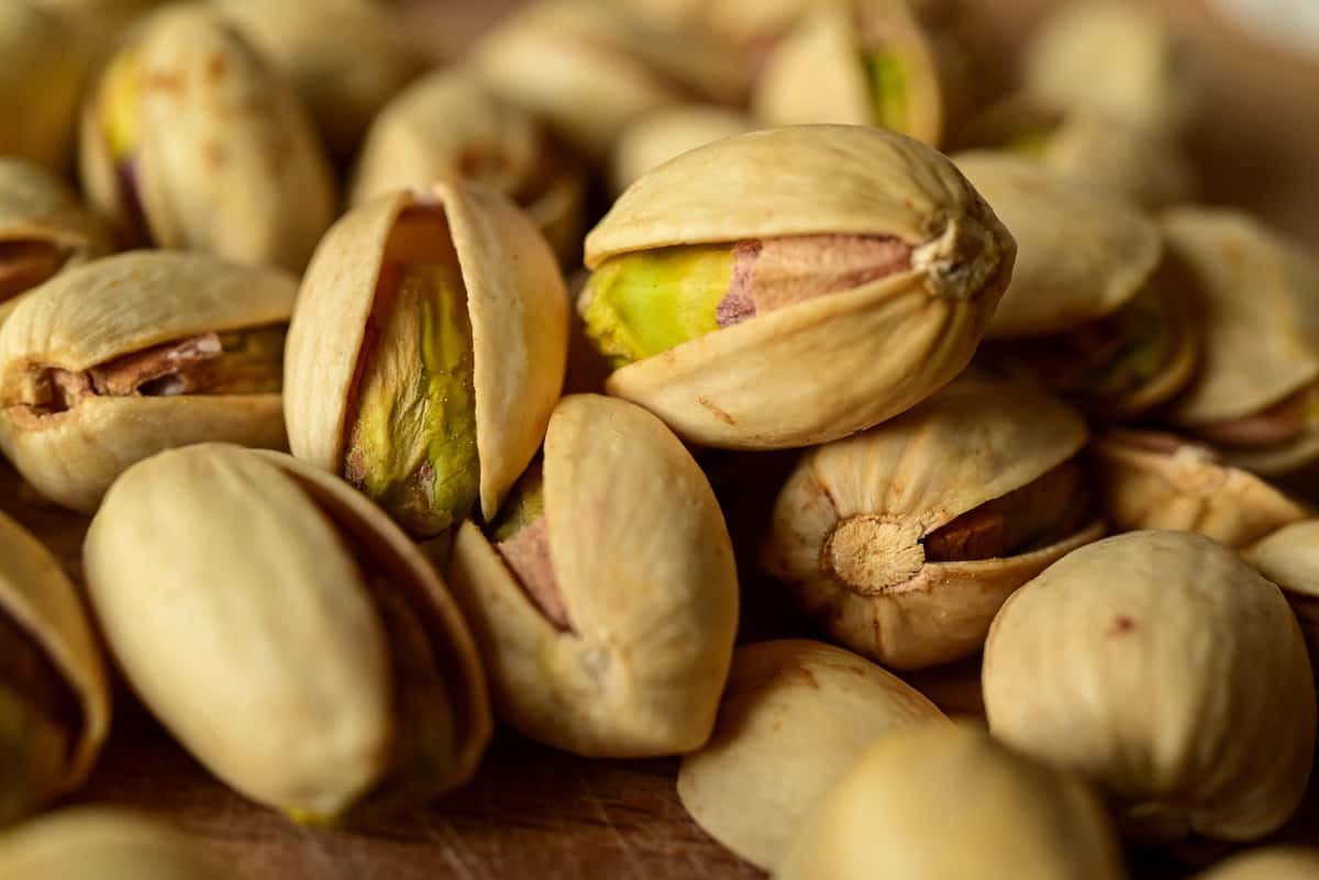 Close-up of roasted pistachios in their shells, showcasing their green centers and natural beige outer shells.