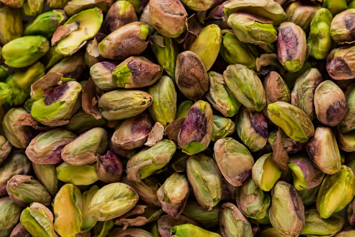 Close-up of raw, shelled pistachios with purple and green hues, showing natural texture and partially removed skins.
