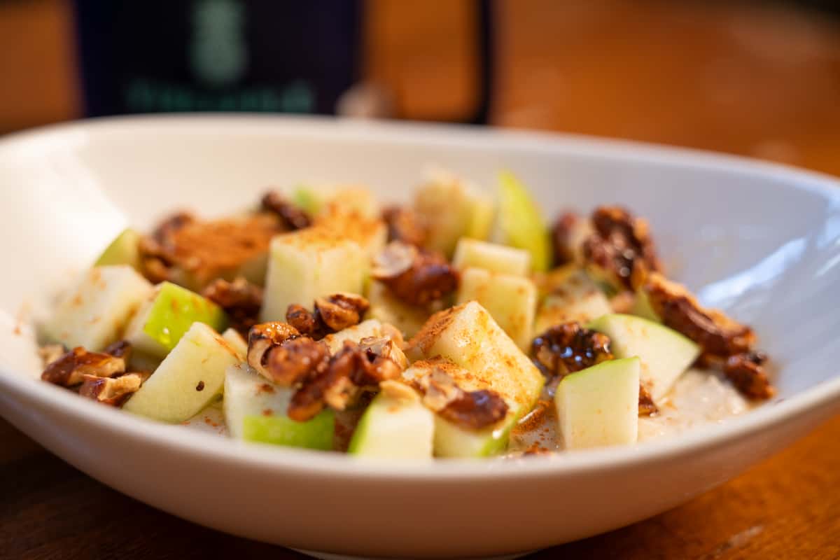 Oatmeal topped with green apple pieces, cinnamon, and granola from a bowl.