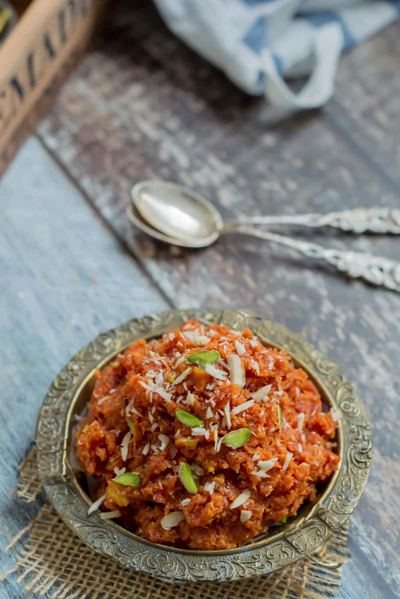 Rich gajar ka halwa topped with sliced almonds and pistachios in an ornate bowl on a rustic tabletop