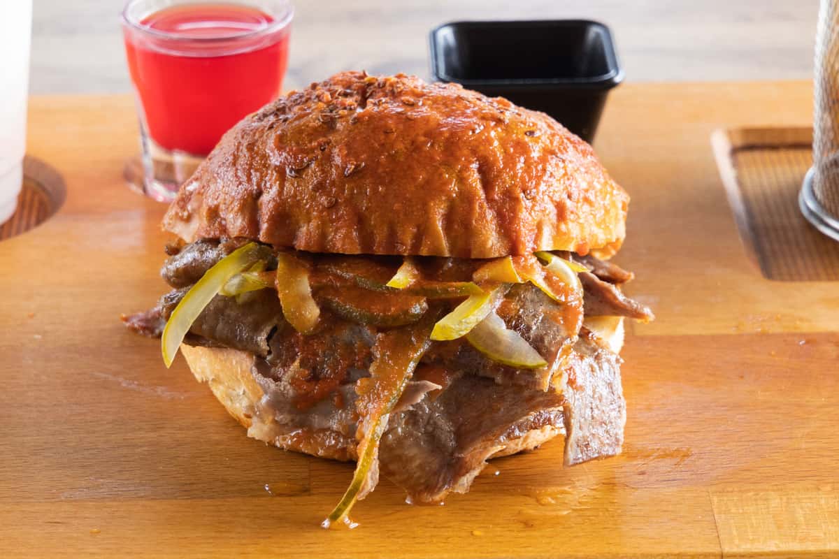 Slow-cooked Mexican pork torta topped with pickled jalapeños, onions, and savory sauce on a toasted artisan bun.