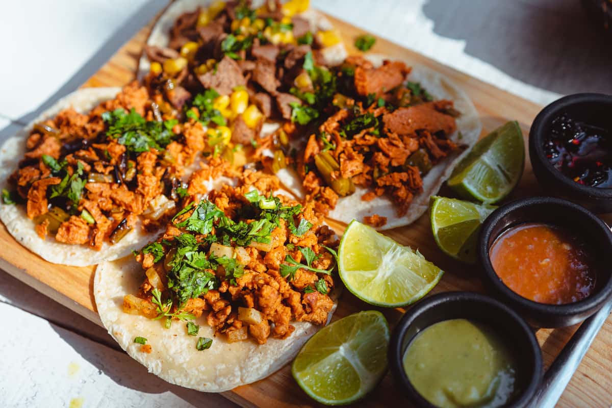 Close-up of street-style tacos topped with seasoned meat, fresh cilantro and onion, served with lime wedges and salsa