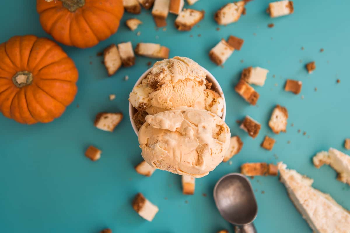 Pumpkin spice ice cream scoops with cake pieces and mini pumpkins on teal background, autumn-themed dessert flat lay