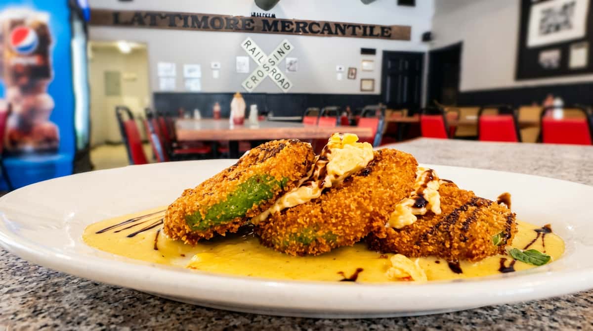 Four pieces of breaded, fried green tomatoes with yellow sauce and a dark drizzle on a white plate in a restaurant.