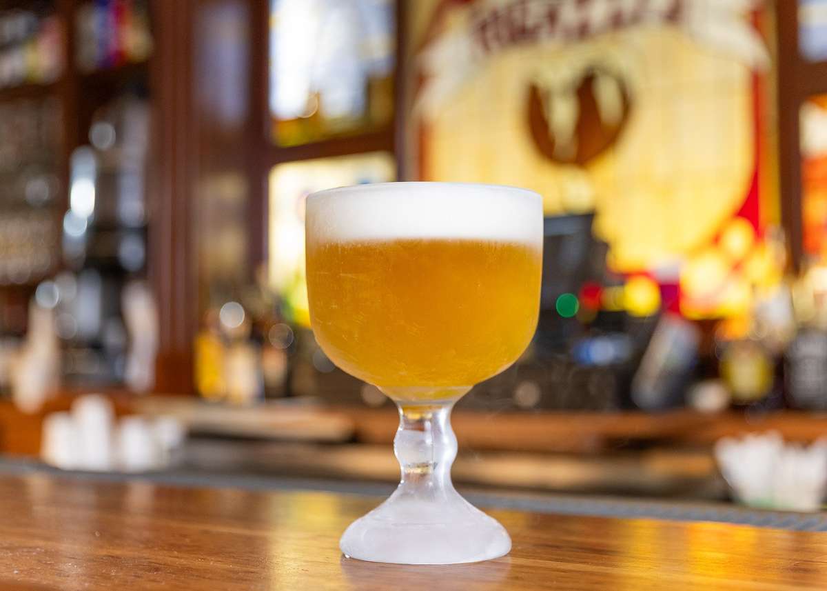 Frosted goblet filled with golden draft beer, topped with a thick foamy head, set on a polished wooden bar.