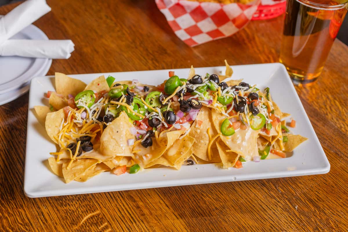 Shareable platter of loaded nachos topped with cheese, vegetables, and savory toppings.