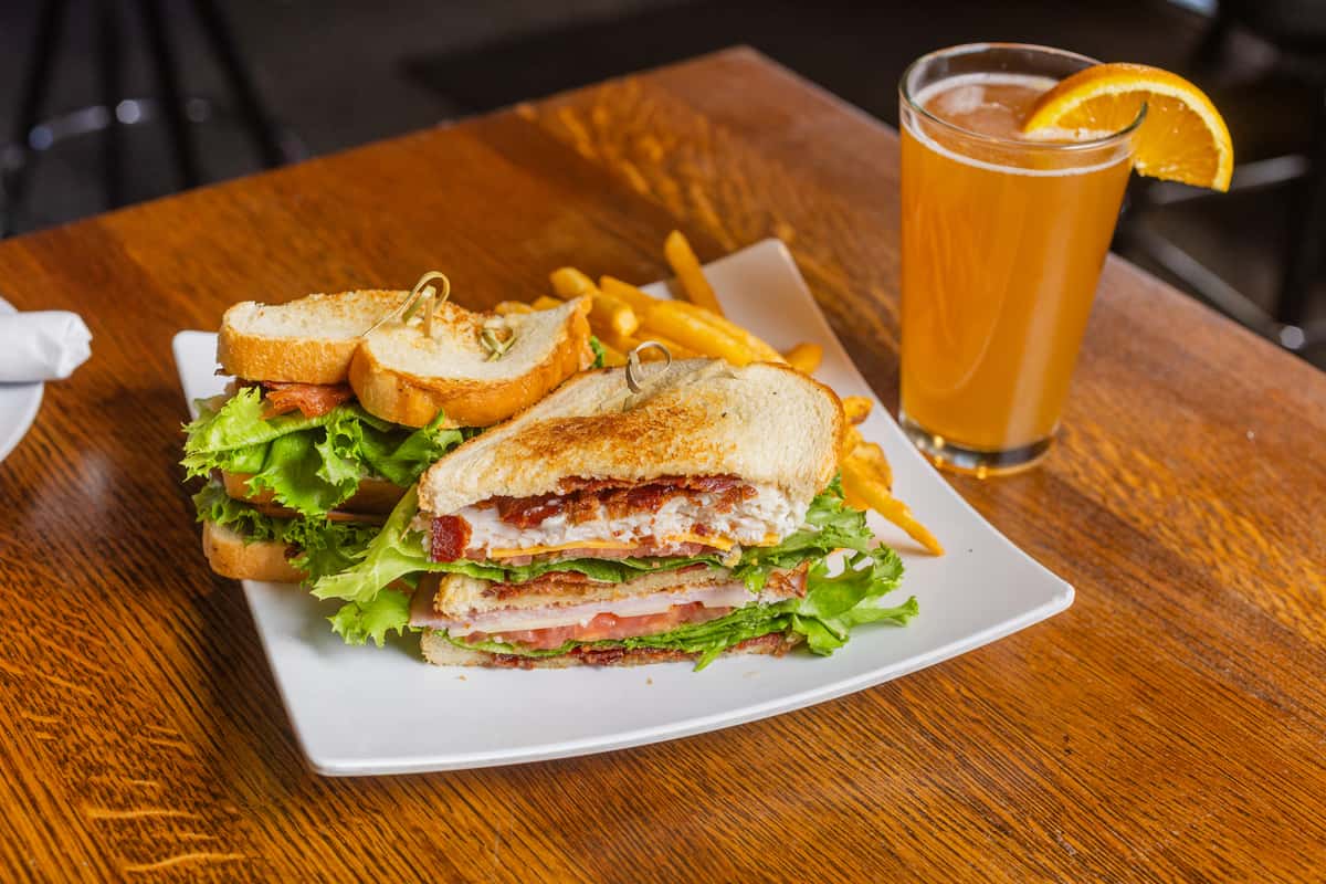 Classic club sandwich served with house-made chips and a refreshing beer in a casual pub setting.