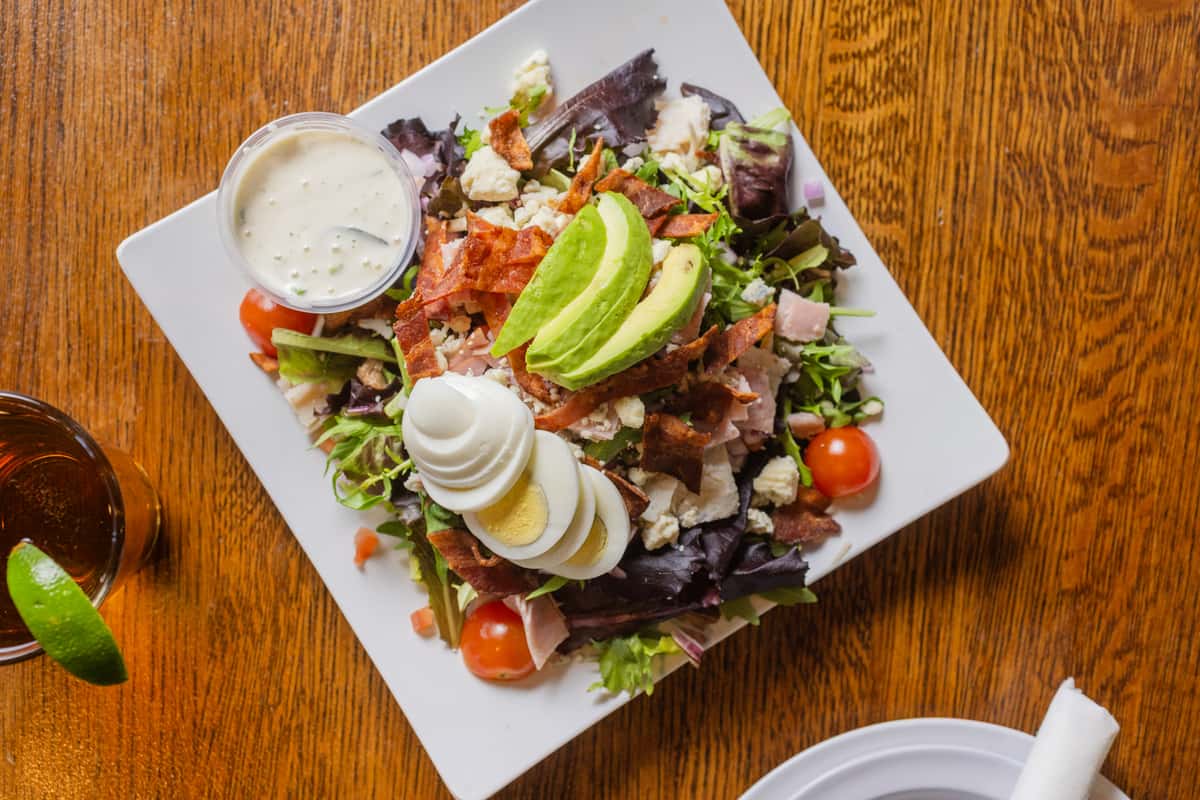 Overhead view of a fresh Cobb salad with avocado, hard-boiled eggs, tomatoes, and mixed greens.