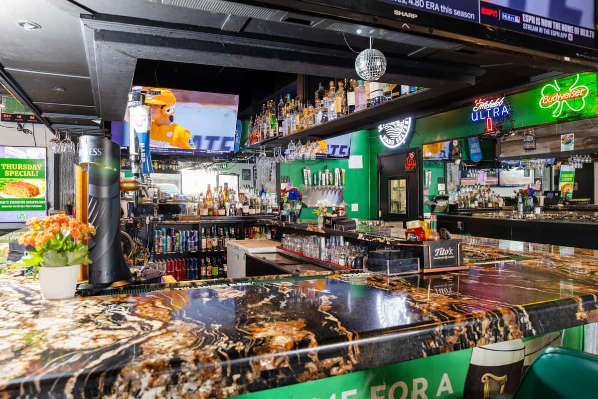 Sports bar interior featuring a polished stone bar, multiple TVs, draft beer selection, and a lively game-day atmosphere.