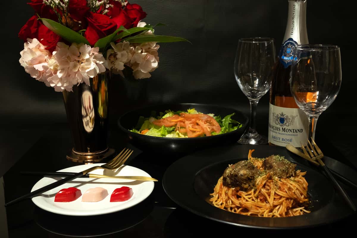 Romantic dinner setting with spaghetti and meatballs, salad, Brut Rosé, floral centerpiece, and heart-shaped desserts.