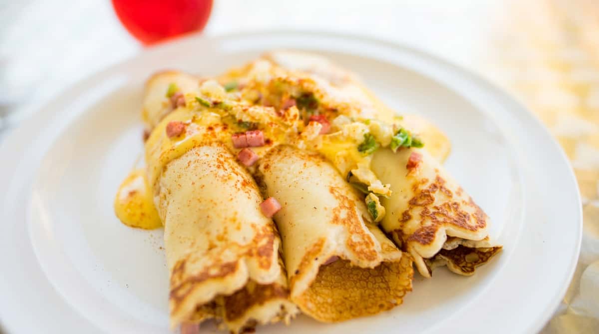 Crepes with a creamy sauce, diced ham, and green onions on a white plate.