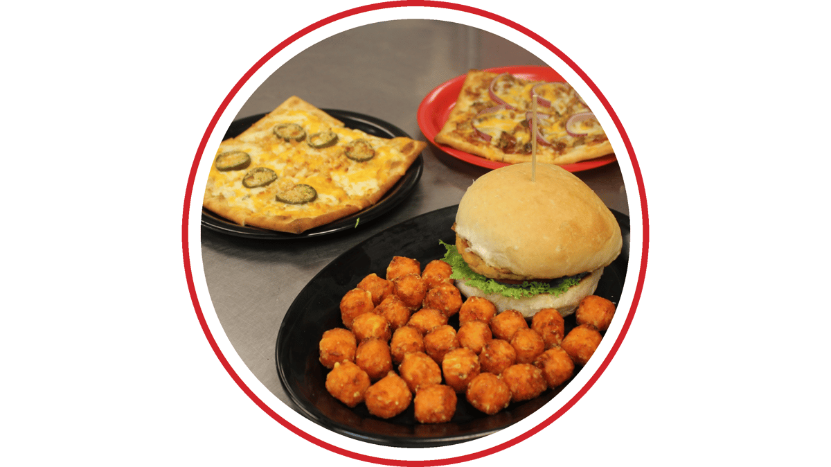 Crispy chicken sandwich with tater tots served alongside specialty flatbread pizzas in a casual restaurant setting.