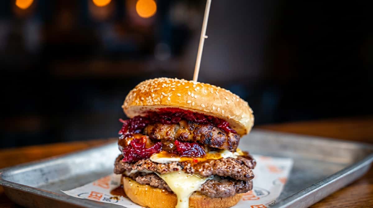 Double cheeseburger with two patties, melted cheese, and a dark red relish, served on a sesame seed bun.