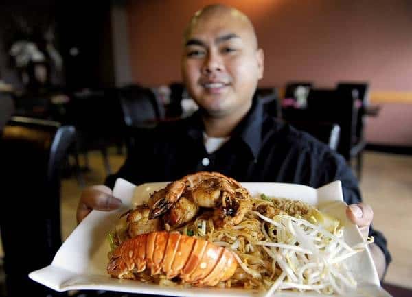 Restaurant owner holding a plate of food containing seafood, bean sprouts and fried rice