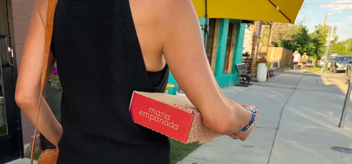 woman carrying takeout box of empanadas