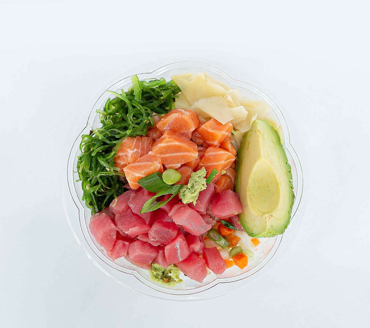 Here's a top-down shot of a custom poke bowl. The bowl is filled with tuna, salmon, avocado, seaweed salad, and pickled ginger.