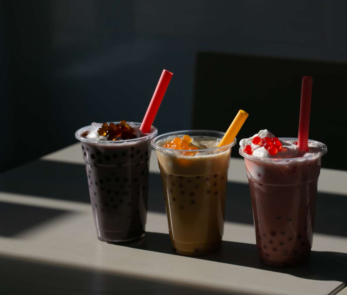 Three bubble teas in clear plastic cups, each with different toppings. The teas have red, orange, and yellow straws, ideal for web design use.