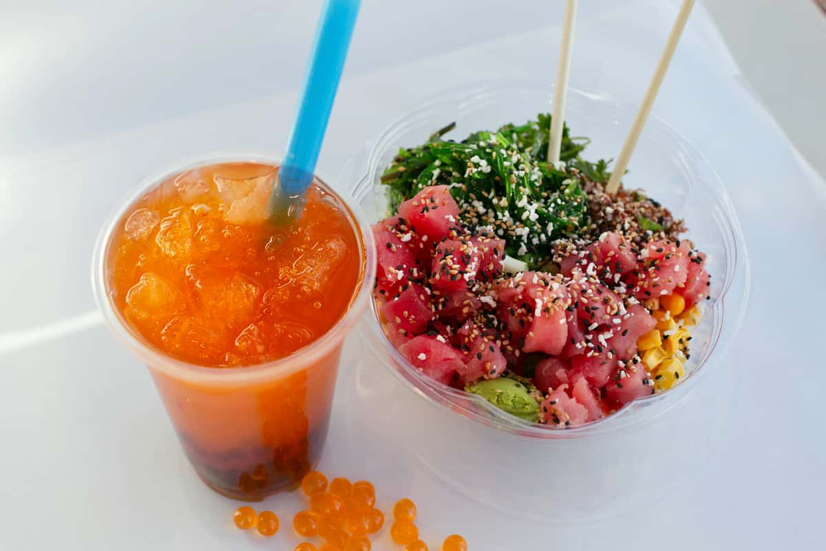 A poke bowl with tuna, seaweed salad, corn, and avocado sits next to a drink with boba. The food is brightly colored and looks fresh and tasty.
