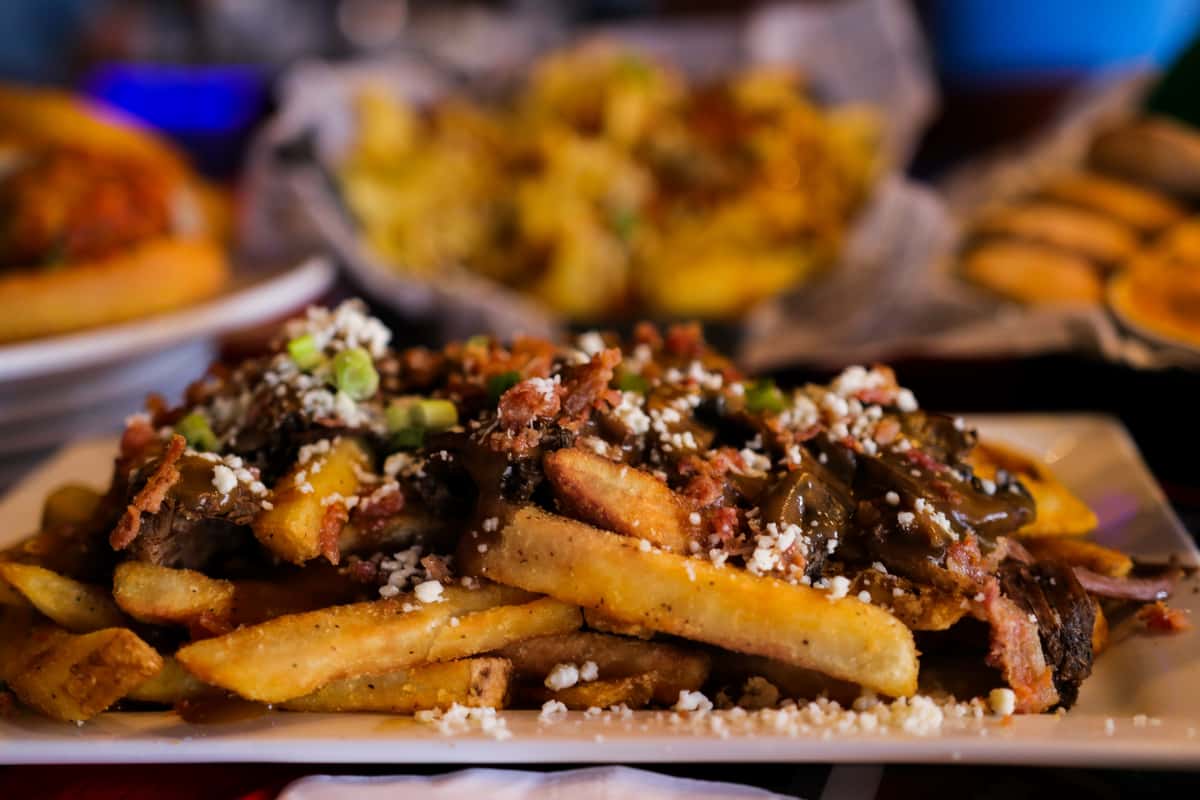 Loaded fries topped with slow-smoked brisket, savory gravy, crumbled cheese, and green onions, served as a hearty comfort food appetizer at The Boxer Kitchen & Bar.