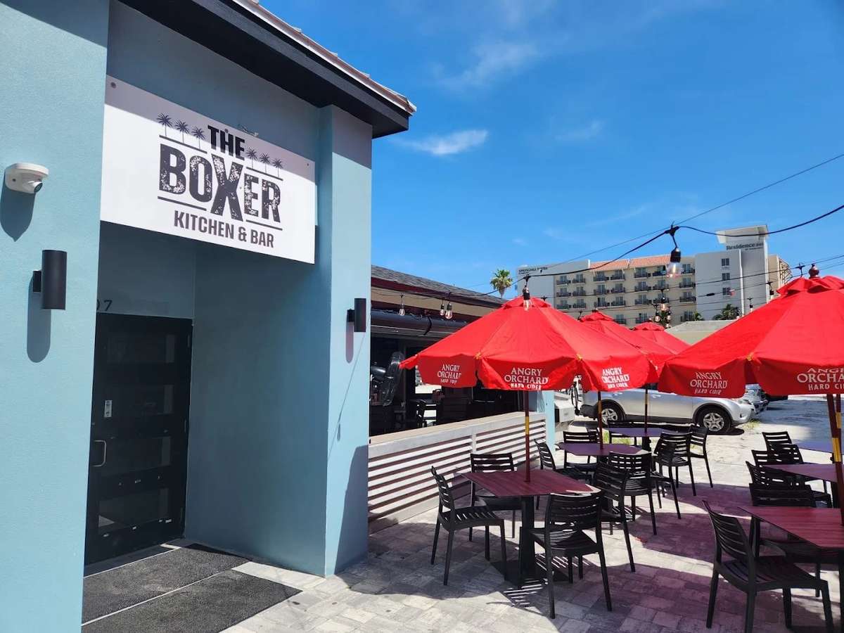Outdoor patio seating at The Boxer Kitchen & Bar featuring shaded tables, bright red umbrellas, and a casual open-air dining atmosphere in Clearwater Beach, Florida.