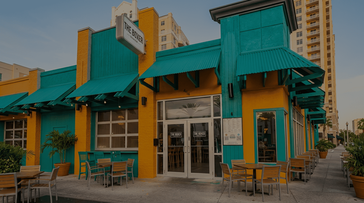 storefront-exterior_enhanced.png: The Boxer restaurant exterior with orange stucco, teal wooden siding, green awnings, and an outdoor dining area.
