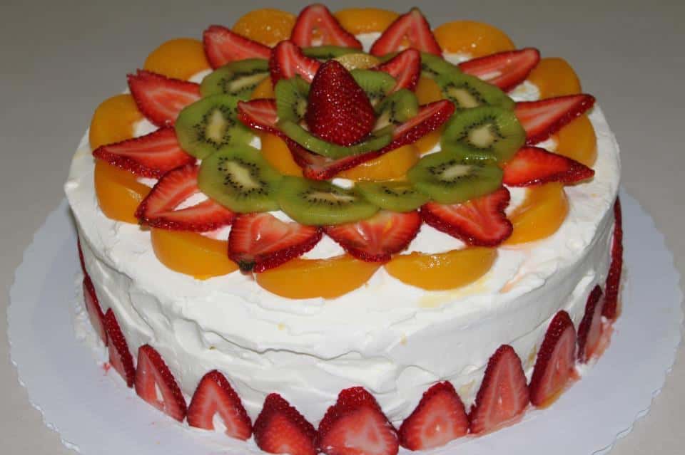 Cake with white icing topped with peaches, strawberries and kiwi slices