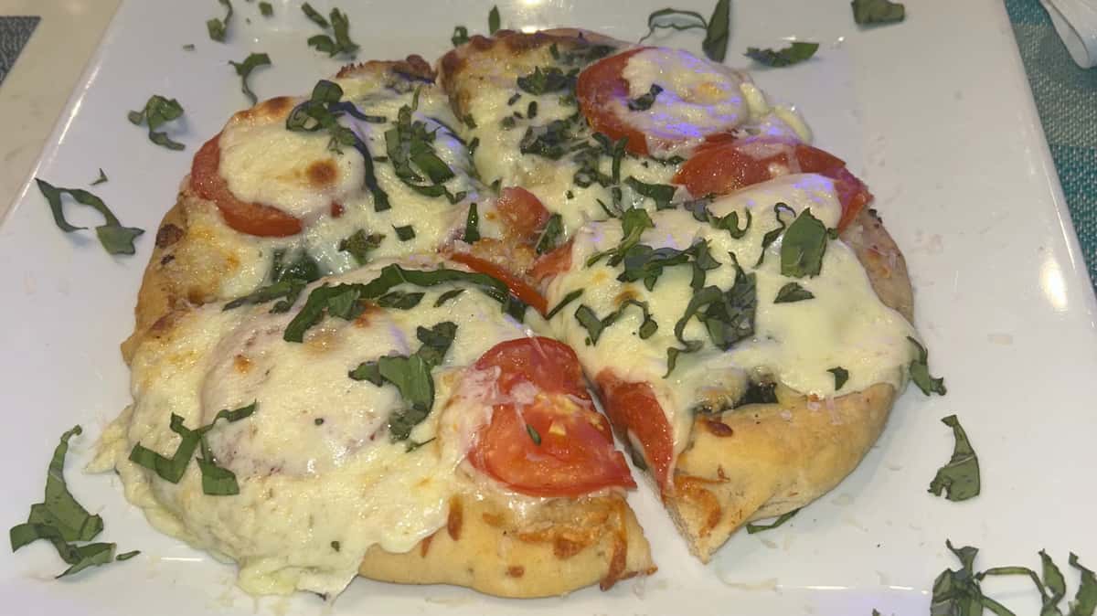 Flatbread pizza topped with melted cheese, tomatoes, and fresh herbs.
