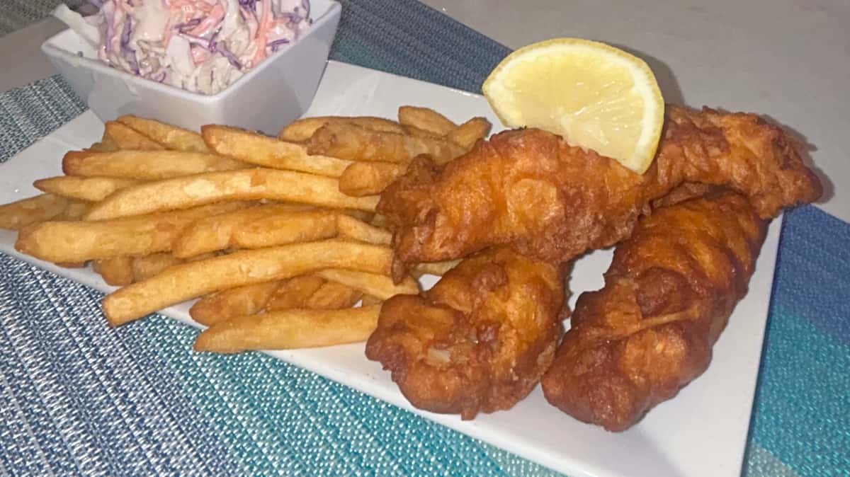 Plate of fried fish with French fries and a lemon wedge.