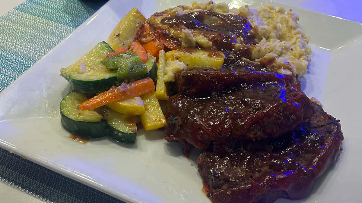 Grilled steak served with sautéed vegetables and rice on a white plate.