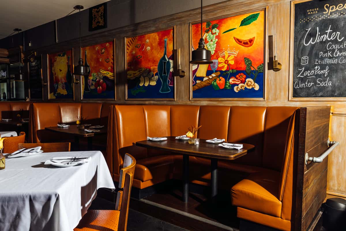 cozy restaurant interior with leather booth seating, white tablecloth tables, and colorful wall art creating a warm upscale dining atmosphere