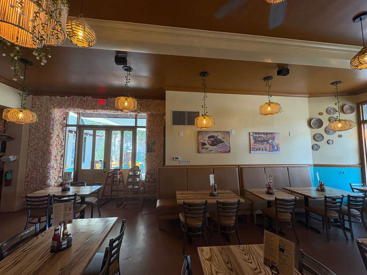 Cozy dining area with wood tables, woven pendant lights, floral entryway, and colorful wall decor in a vibrant Mexican restaurant.