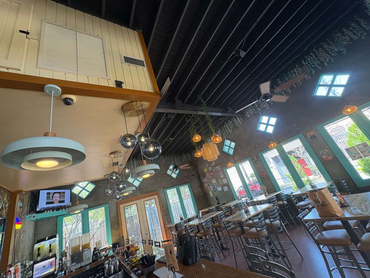 Chic Mexican cantina with turquoise window frames, modern lighting, floral ceiling decor, and casual dining tables.
