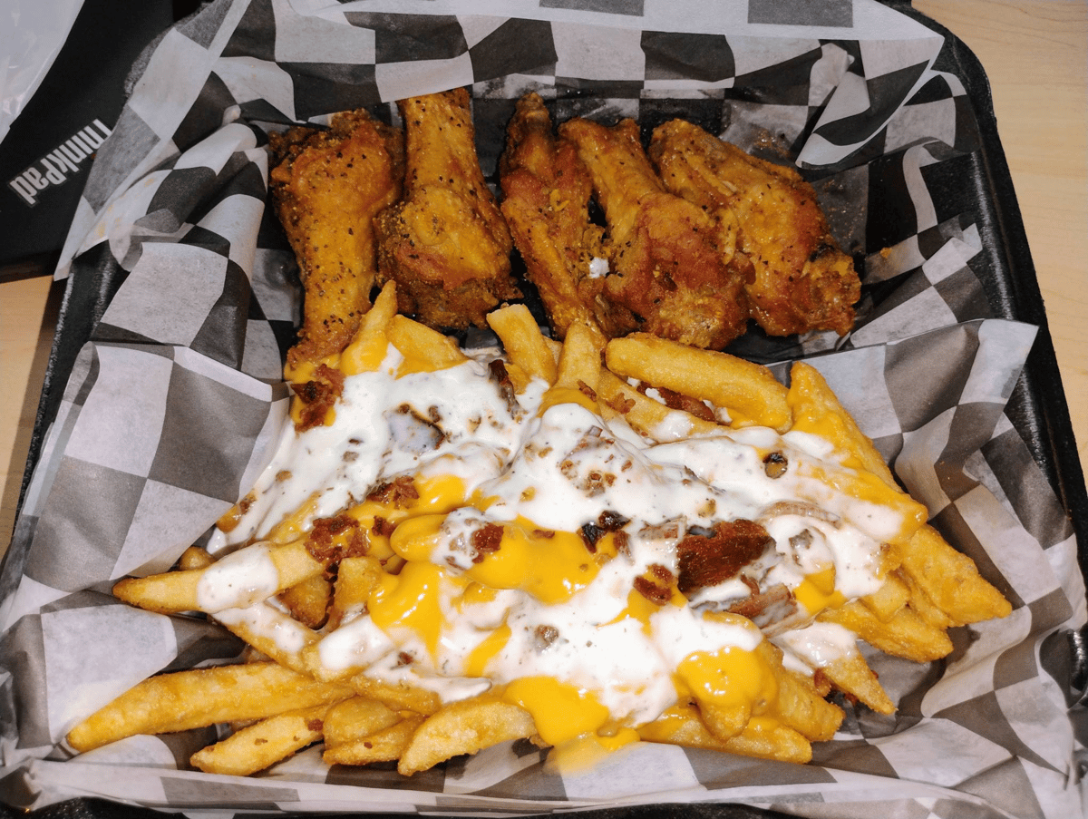 Crispy chicken wings served with seasoned fries topped with melted cheese, ranch dressing, and bacon bits.