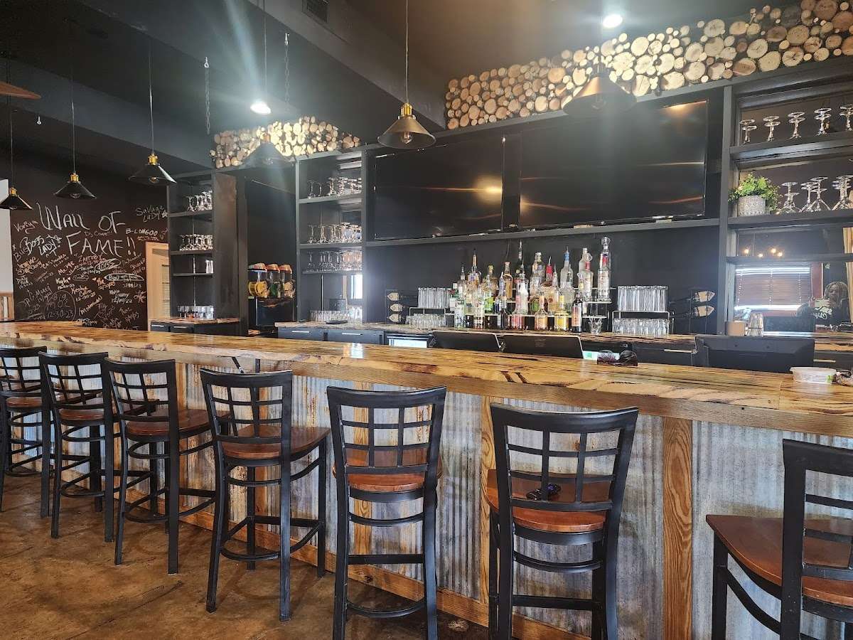 Rustic bar with wood and corrugated metal design, stocked shelves, a chalkboard "Wall of Fame," and high-top seating.