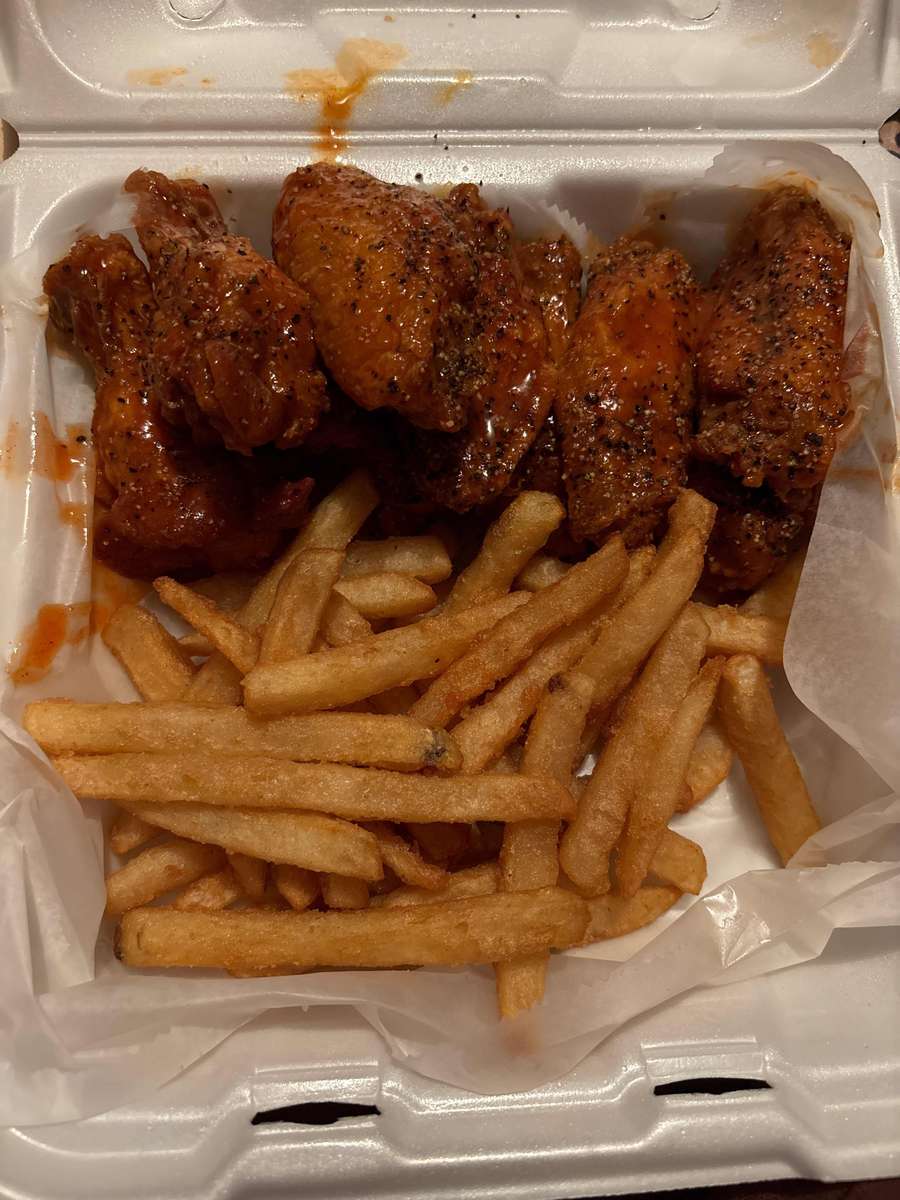 Takeout box with seasoned buffalo wings and a generous serving of golden, crispy French fries.