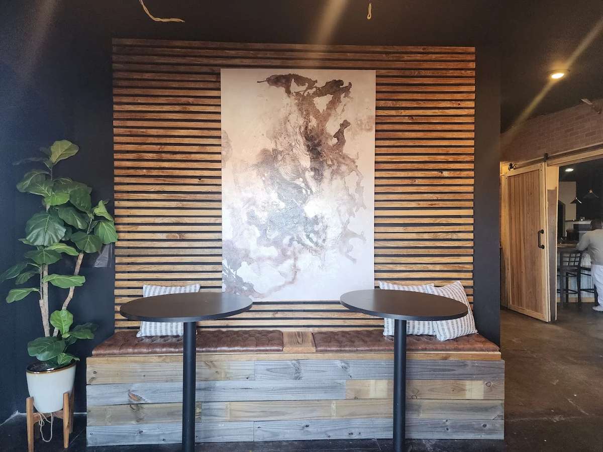 Stylish café seating area with a wooden bench, round tables, abstract wall art, and a potted plant adding a touch of greenery.