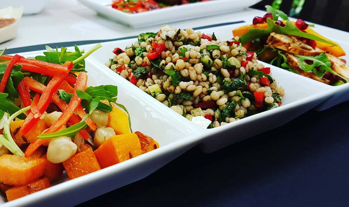 Fresh salads and grain dishes arranged on serving platters for catering or buffet service.