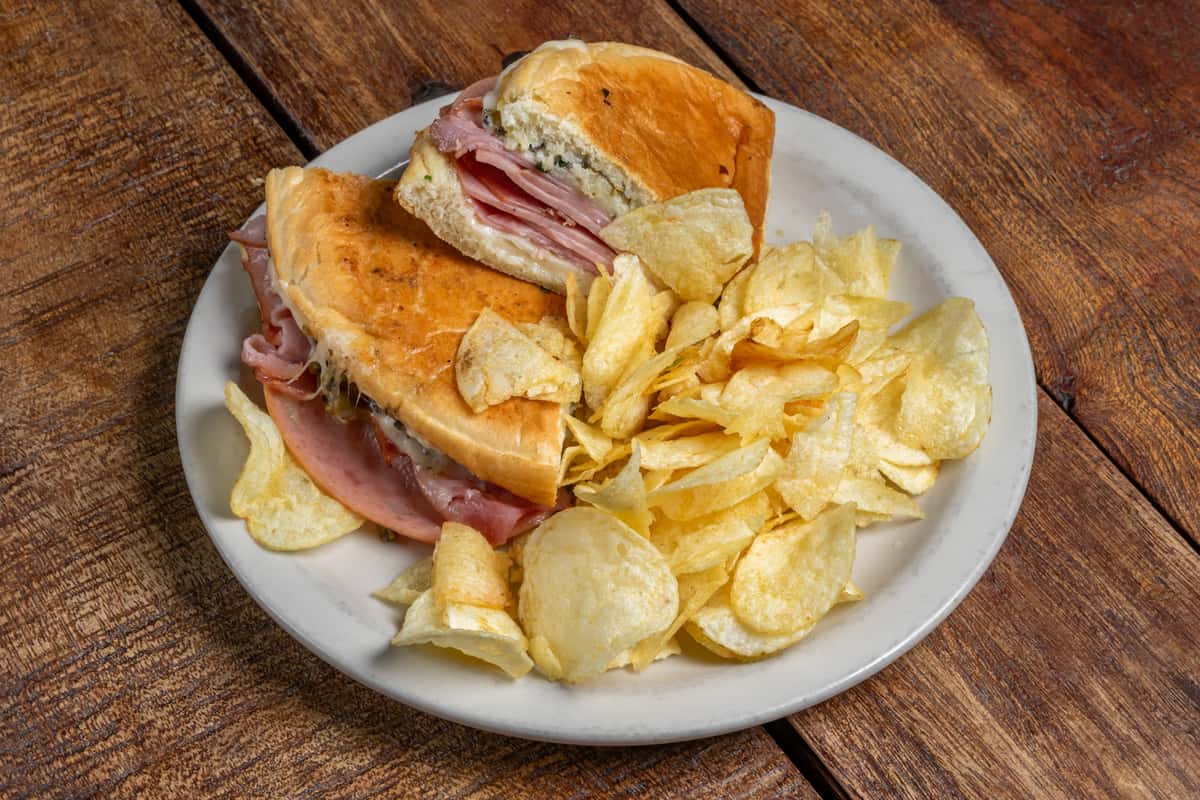 Pressed ham sandwich and golden potato chips on a white plate from The Downing Bottles and Bites.